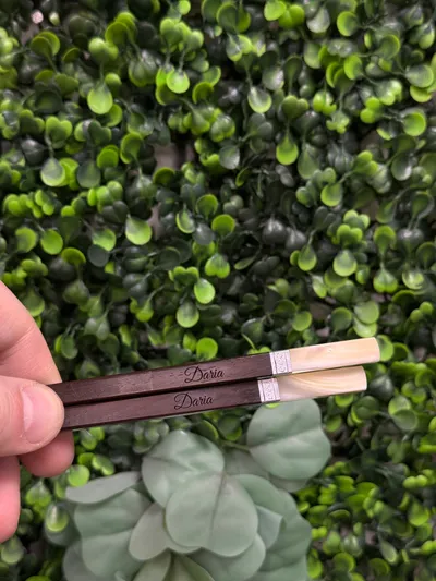 Zwei dunkle Holz-Essstäbchen mit graviertem Vornamen in Schreibschrift