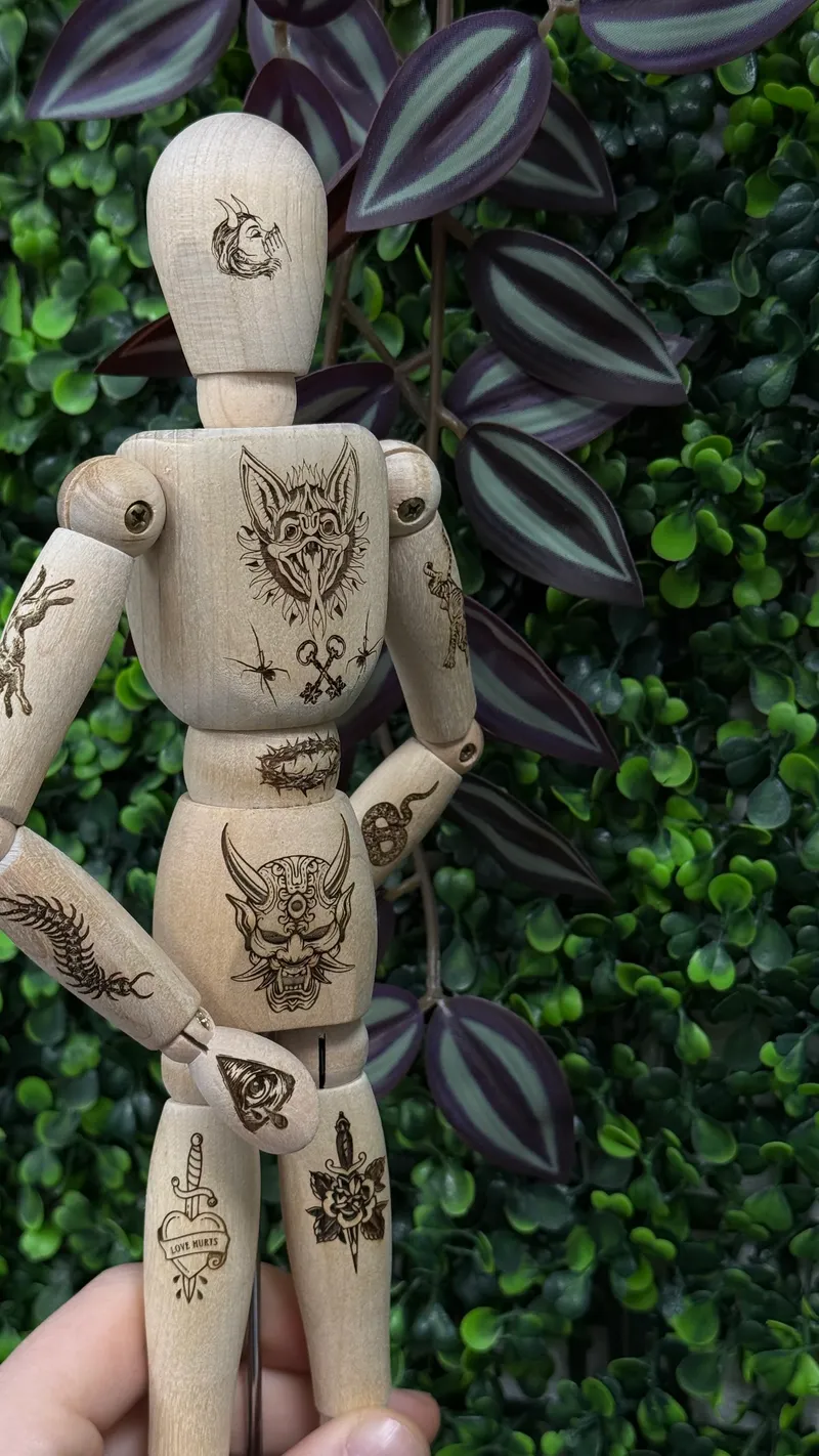 Hölzerne Gliederpuppe mit fein gravierten Tattoo-Motiven auf Armen, Kopf und Körper