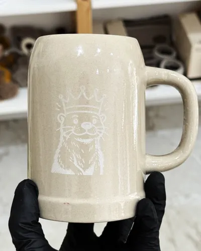 Keramik-Bierkrug mit graviertem Otter mit Krone, mit Handschuhen gehalten