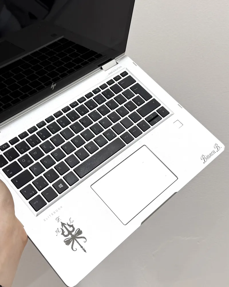 Aufgeklappter silberner Laptop mit graviertem Namenszug und Ornament auf der Handablage