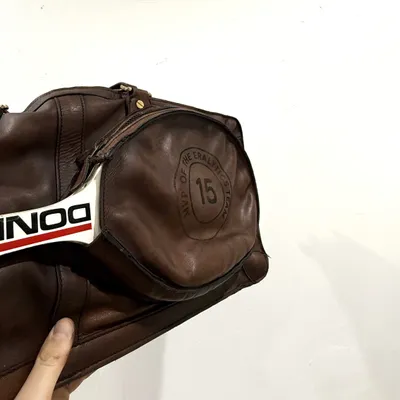 Braune Ledertasche mit rund gravierter Prägung und großer Zahl auf dem Seitenteil