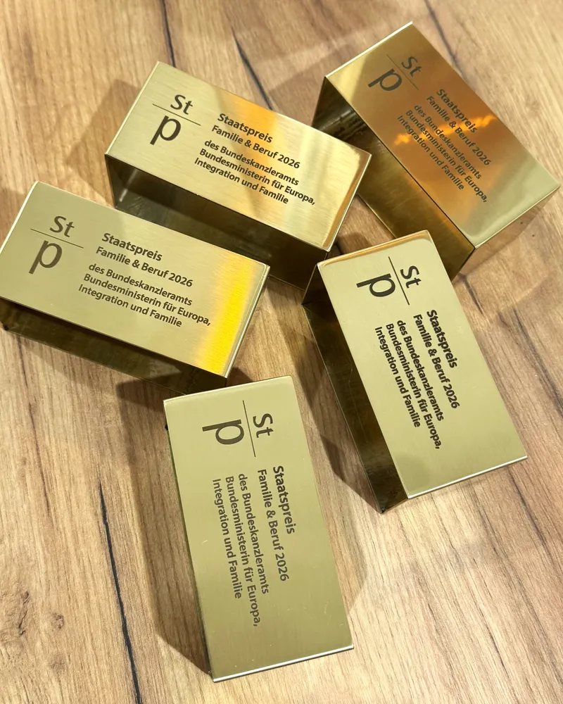 Fünf goldfarbene Award-Quader mit graviertem Logo und Preistext, auf Holztisch