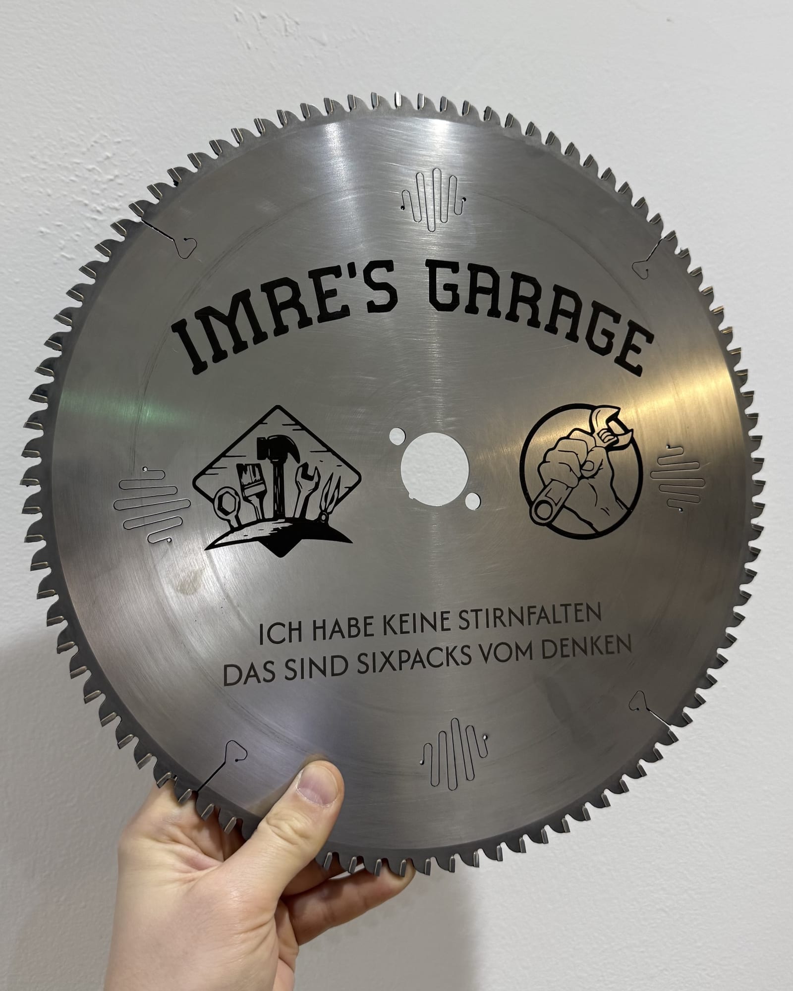 Kreissägeblatt mit graviertem Werkstattnamen, Werkzeugmotiven und Spruch, in der Hand