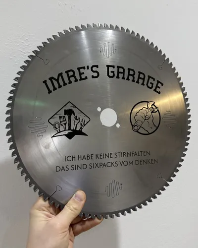 Kreissägeblatt mit graviertem Werkstattnamen, Werkzeugmotiven und Spruch, in der Hand