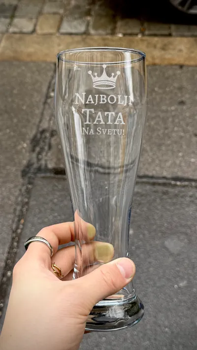 Weizenbierglas mit Krone und graviertem Schriftzug, im Freien in der Hand gehalten